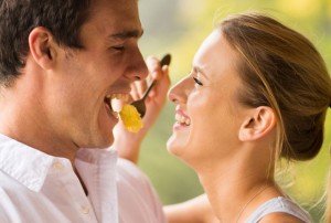 cheerful young woman feeding boyfriend breakfast