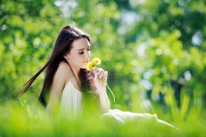девушка в парке сидит на траве и нюхает цветы
