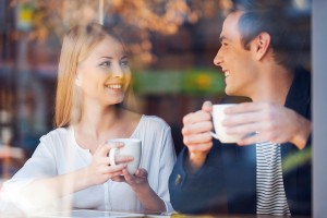 Through a glass shot of beautiful young couple looking at each other and smiling while enjoying coffee in cafe together