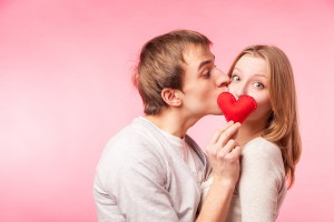 Man kissing girl hiding behind a little red heart