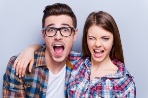 Beautiful young loving couple making faces at camera while standing against grey background