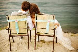 Newlyweds Couple Sitting Near Water On The Beach