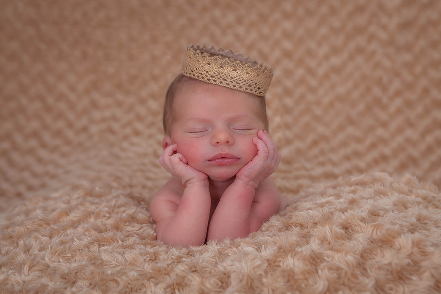 sleeping baby propped on elbows wearing crown.