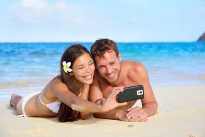 Beach holiday couple taking selfie with smartphone lying down re