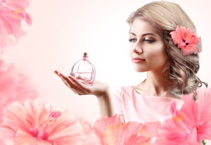Beautiful woman with perfume bottle in flowers on pink backgroun